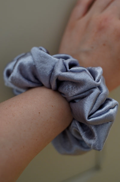 Person wearing a light blue scrunchie on wrist with neutral background