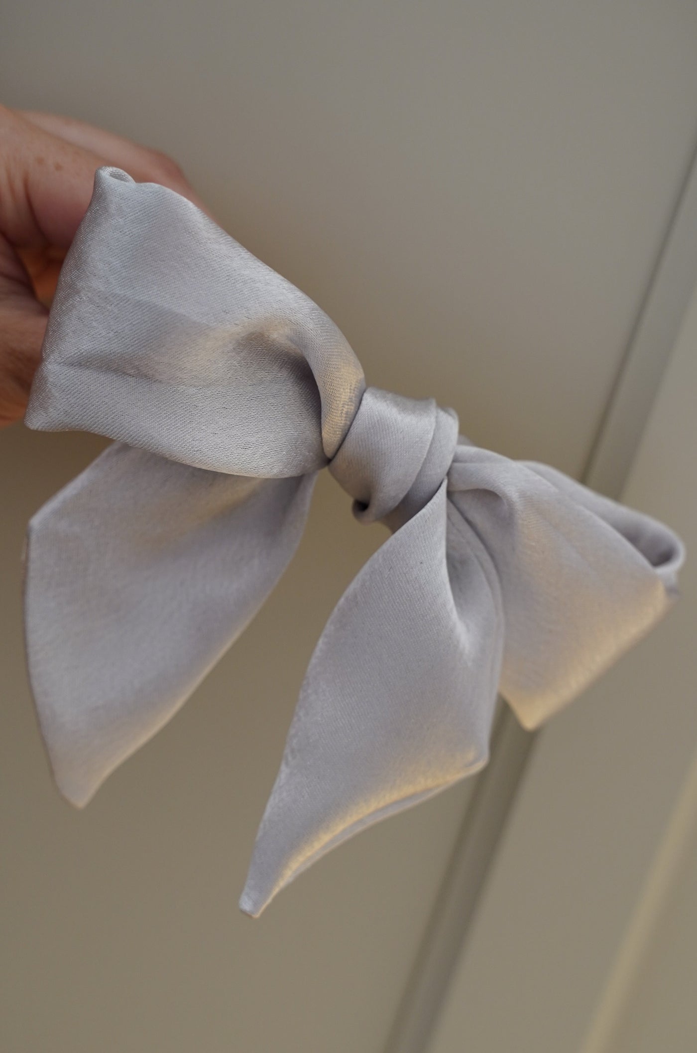 White bow held by a hand against a neutral background